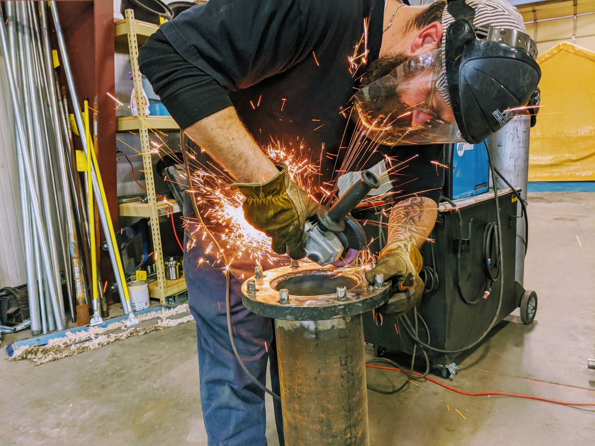 A man is grinding a metal pipe with a grinder in a garage.