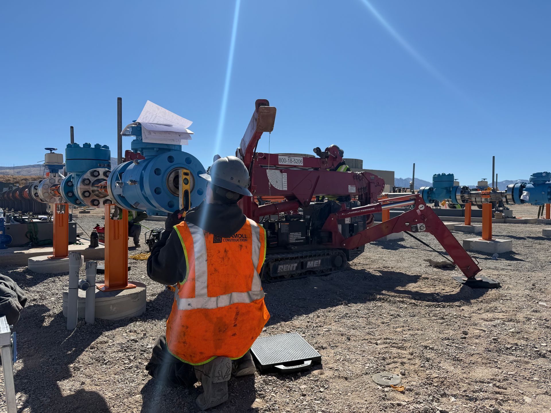 Worker in orange vest standing at a construction site beside drilling machinery and equipment.