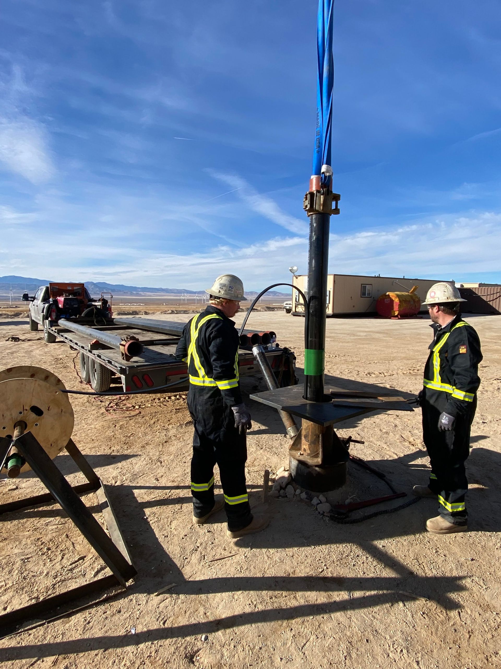 Two men are working on a large pipe in the desert.
