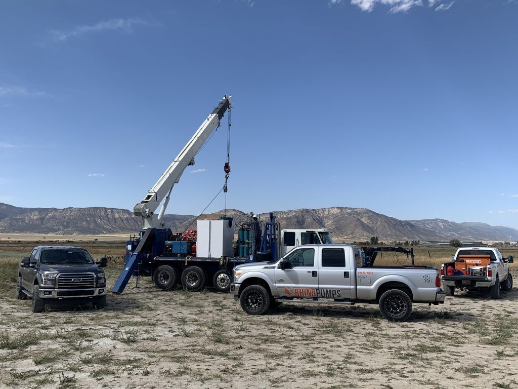 Two trucks are parked next to a crane in a field.