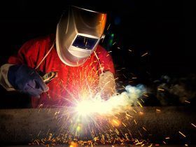 A man wearing a welding helmet is welding a piece of metal.