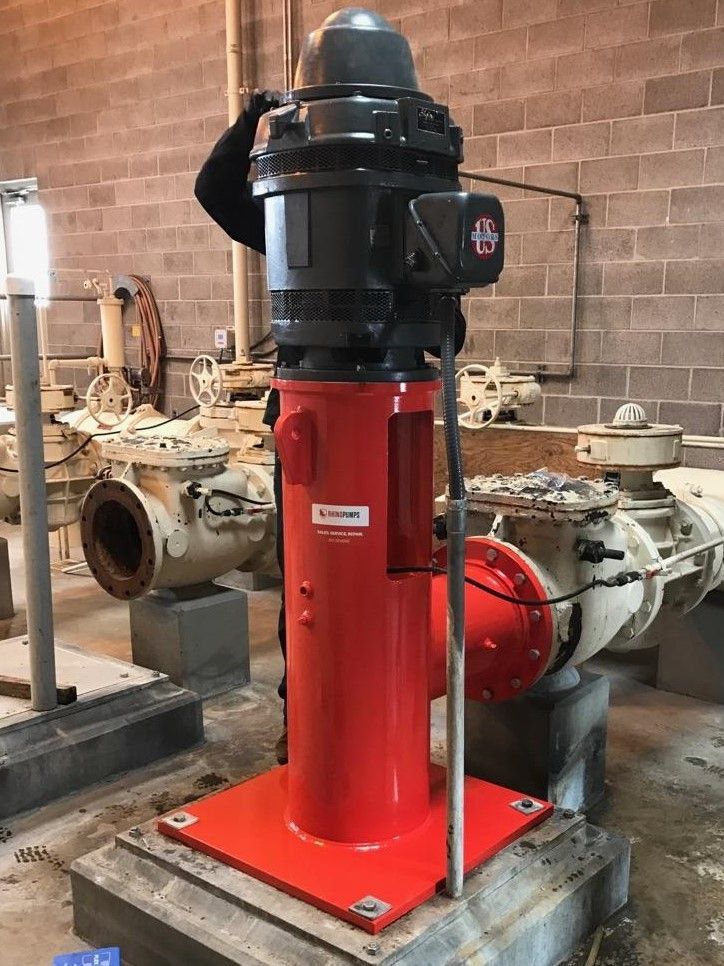 A man is standing next to a red pump in a warehouse.