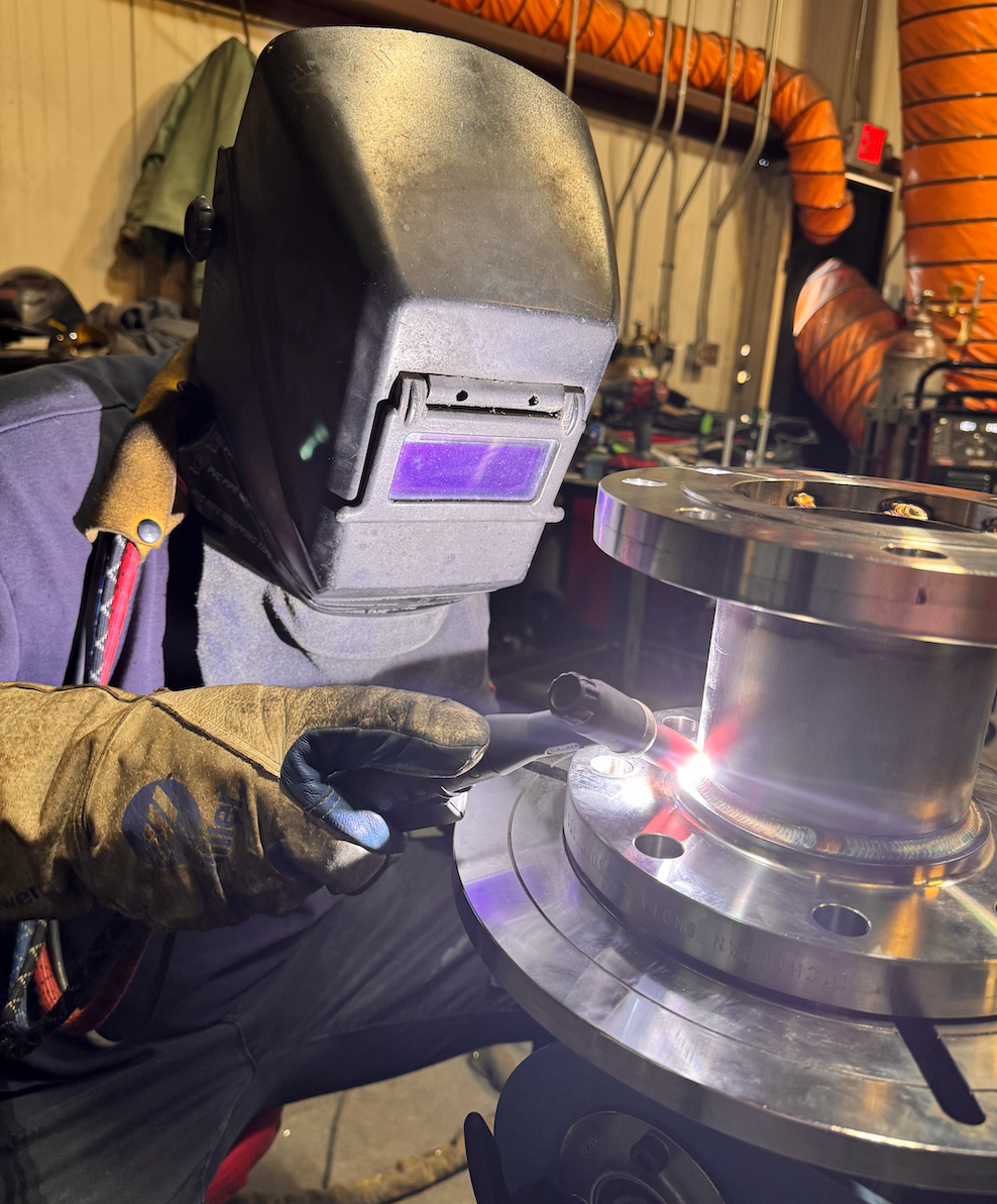 A man wearing a welding helmet is welding a piece of metal