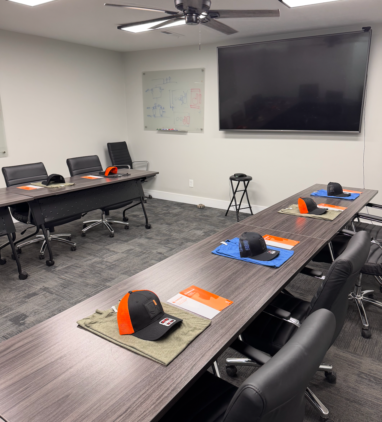 A modern conference room with two long tables, a large TV, and hats laid out for attendees.