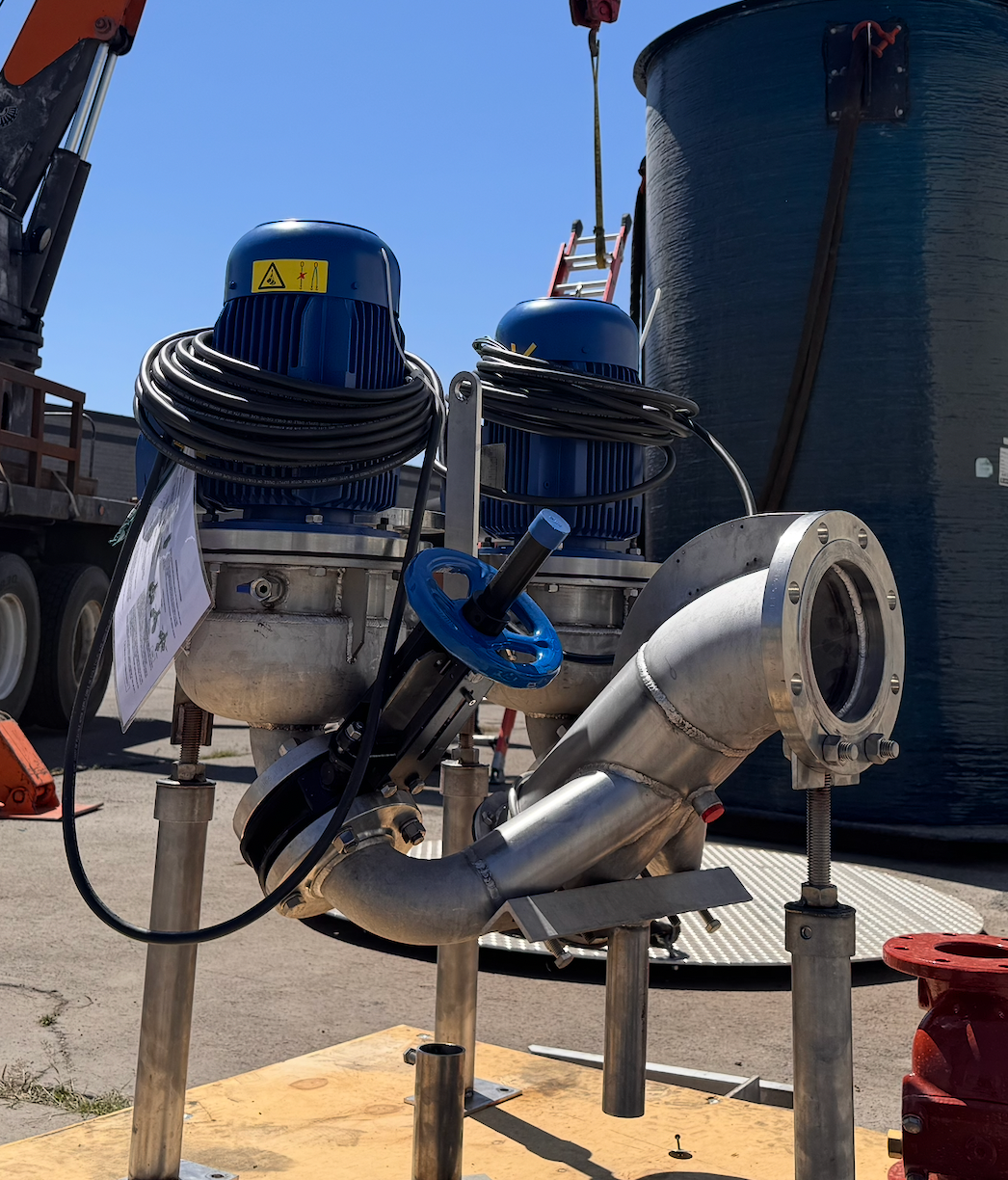 Two blue-topped motors attached to angled metal pipes, standing outside in daylight.