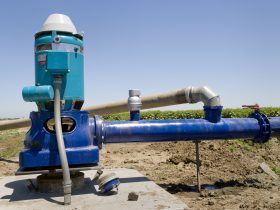 A blue water pump is sitting in the middle of a field.