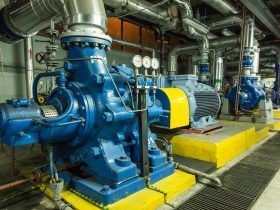 A large blue water pump is sitting in a room filled with pipes.