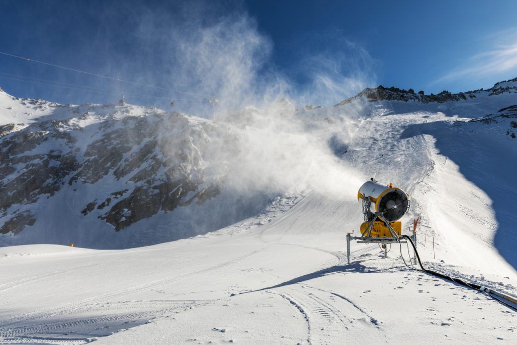 A snow machine is blowing snow on top of a snow covered mountain.