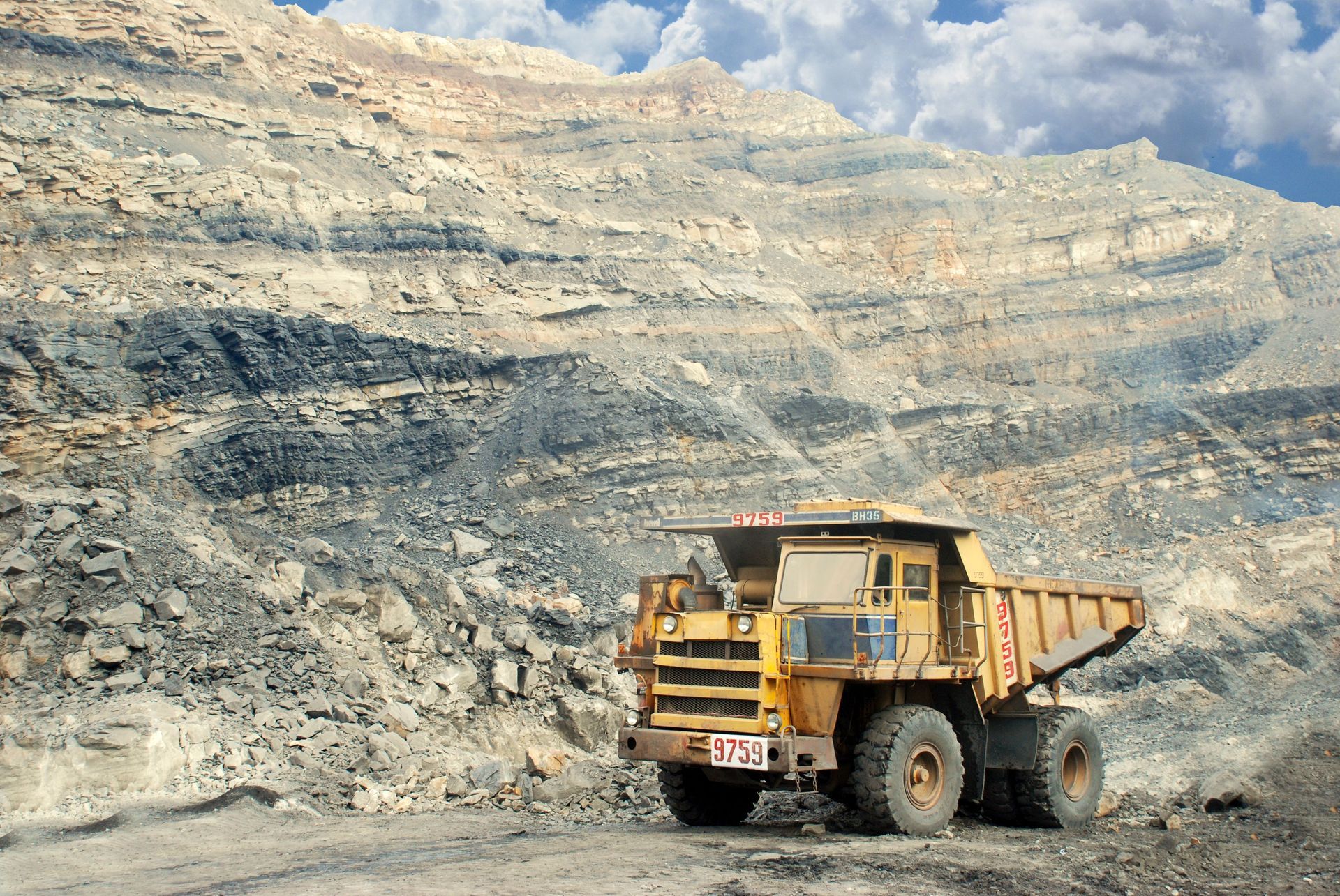 Large yellow dump truck on a rocky open-pit mine under a cloudy sky