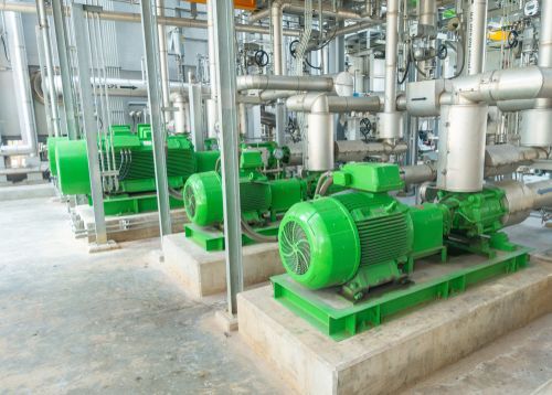 A row of green pumps in a factory with pipes.
