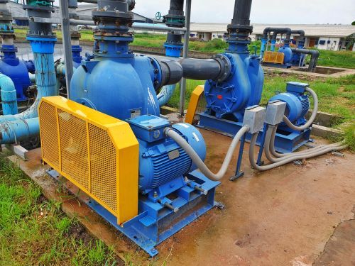 A blue and yellow pump is sitting on the ground next to a bunch of pipes.