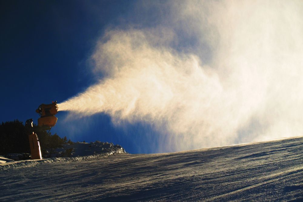 A snow cannon is spraying snow on a snowy slope.
