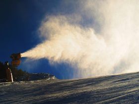 A snow cannon is spraying snow down a snow covered slope.