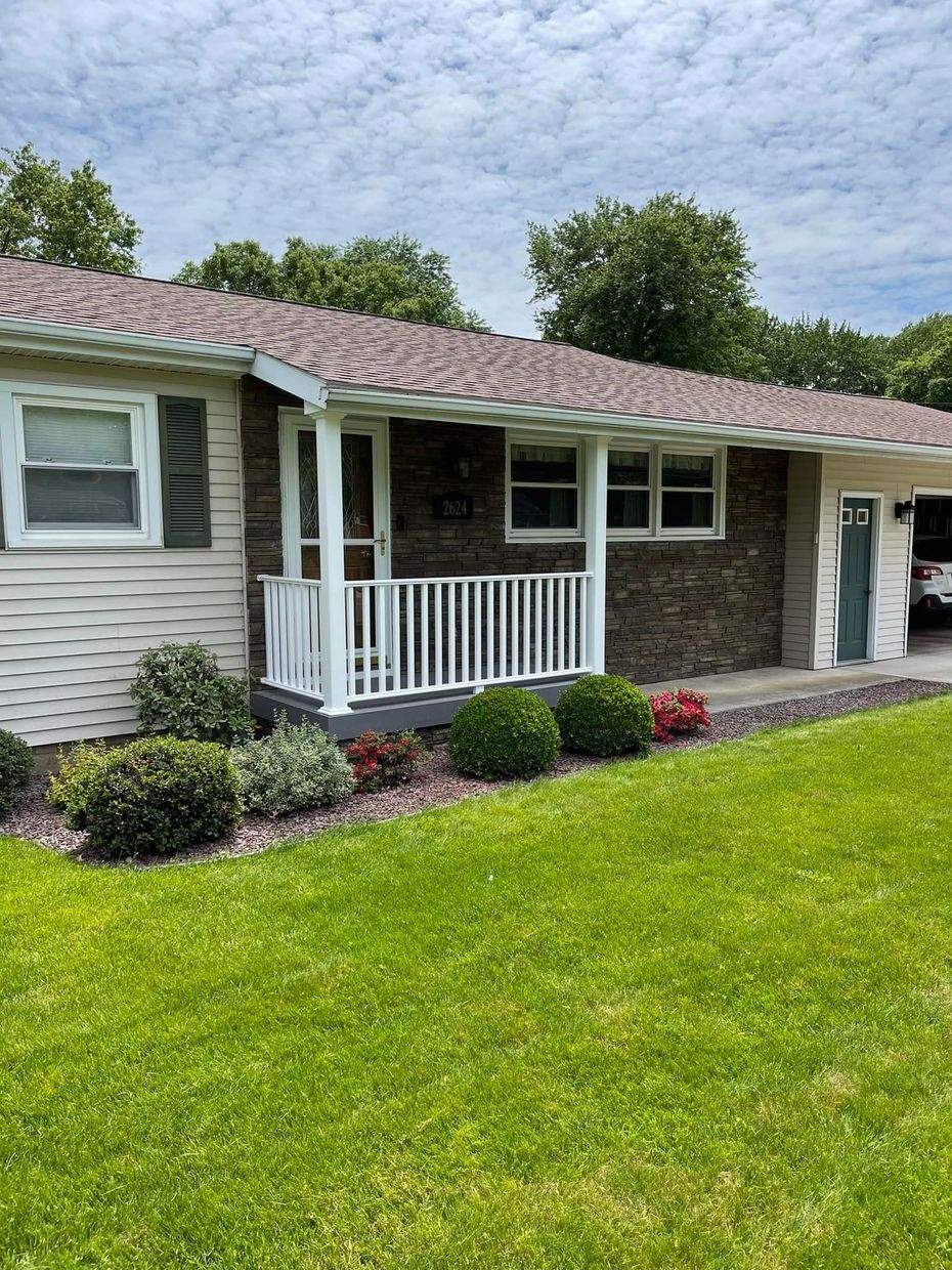 House exterior with white siding, brick accents, a small porch, and a green lawn.