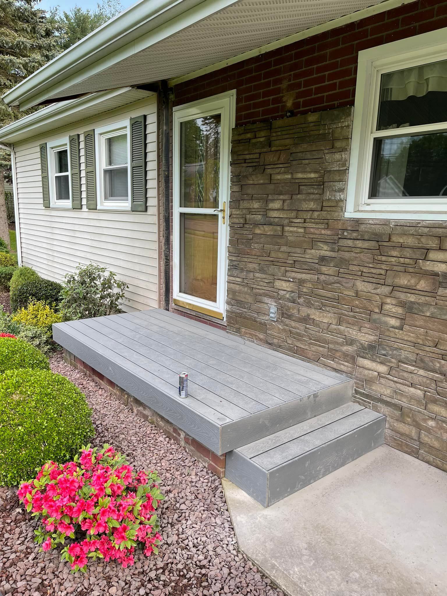 Grey composite steps leading to a home's front door, framed by landscaping and brickwork.