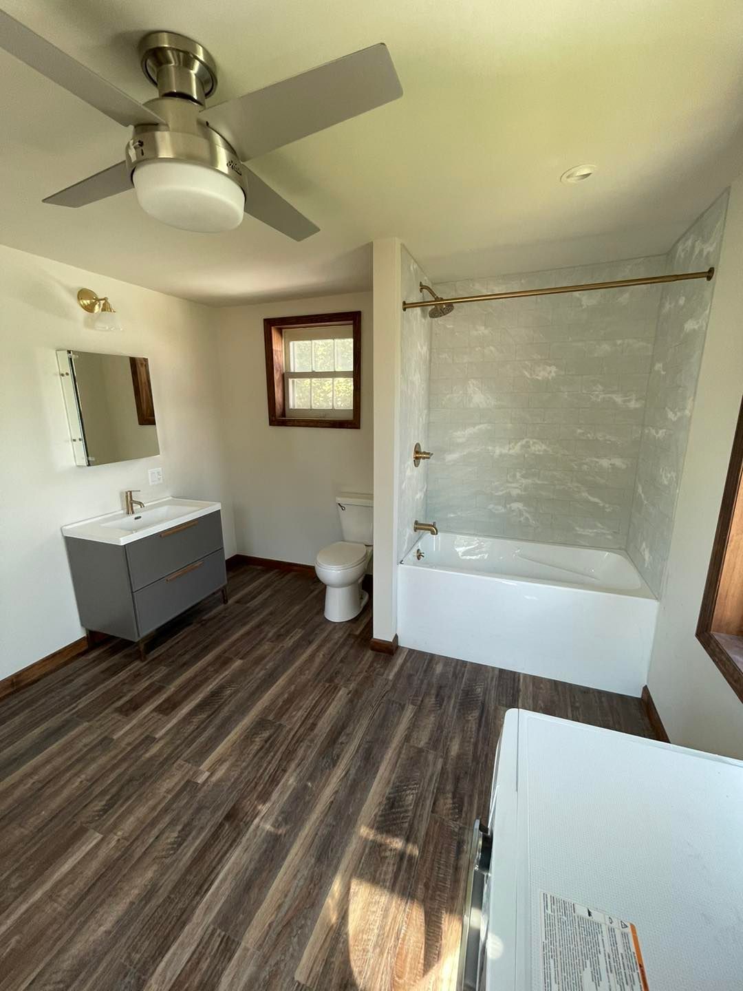 Bathroom with gray vanity, white tub/shower, and wood-look flooring.