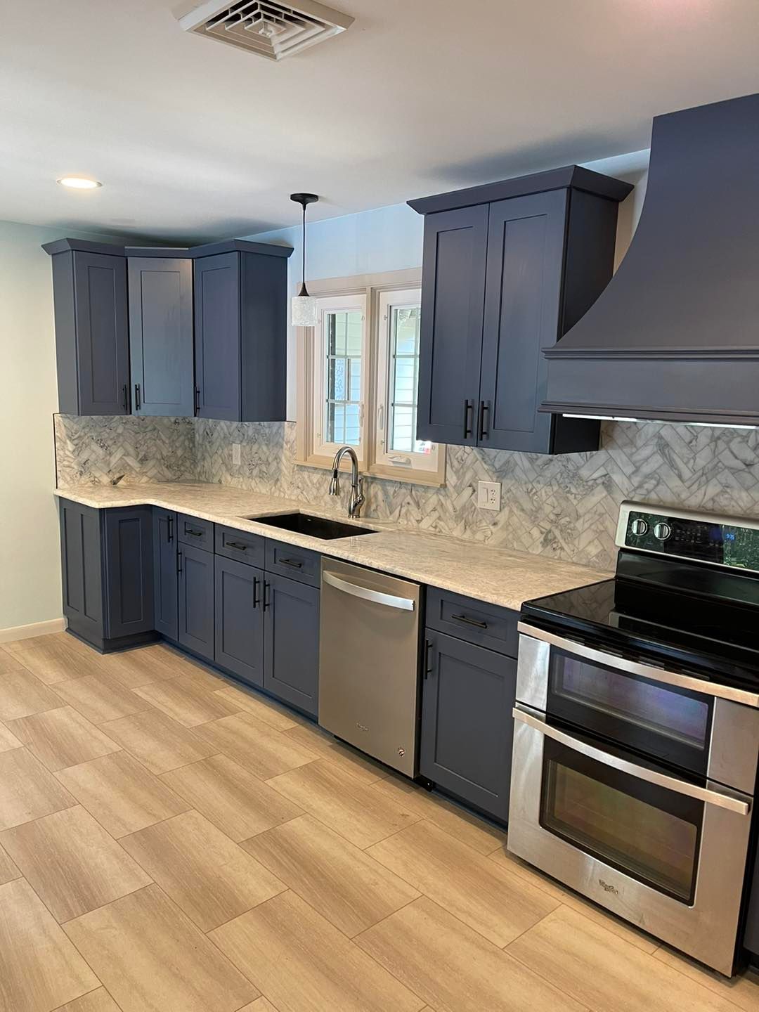 Blue kitchen with light countertops, stainless steel appliances, and light wood-look flooring.
