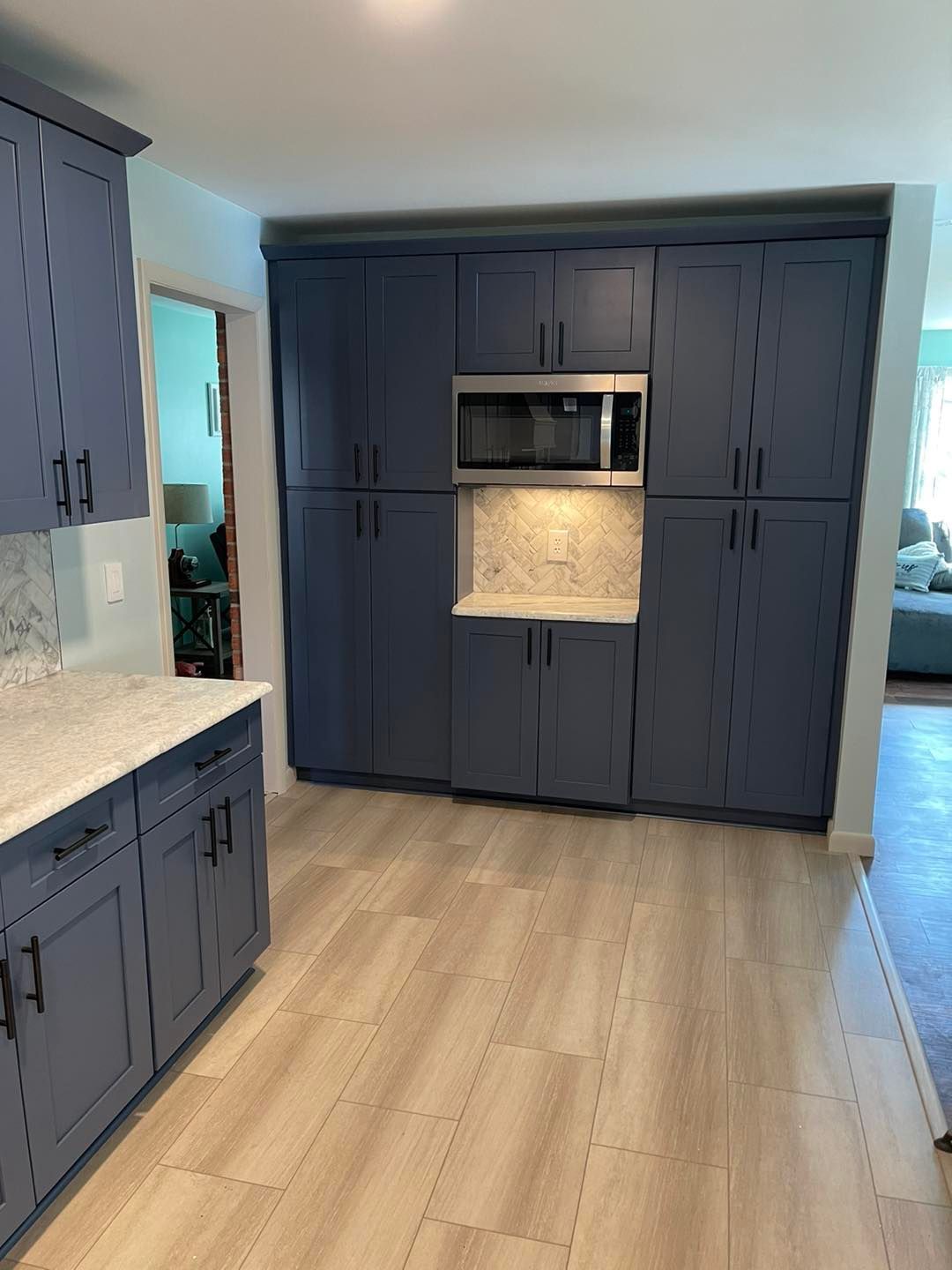 Blue kitchen cabinets with a microwave, light wood-look floors, and a glimpse of a living room.