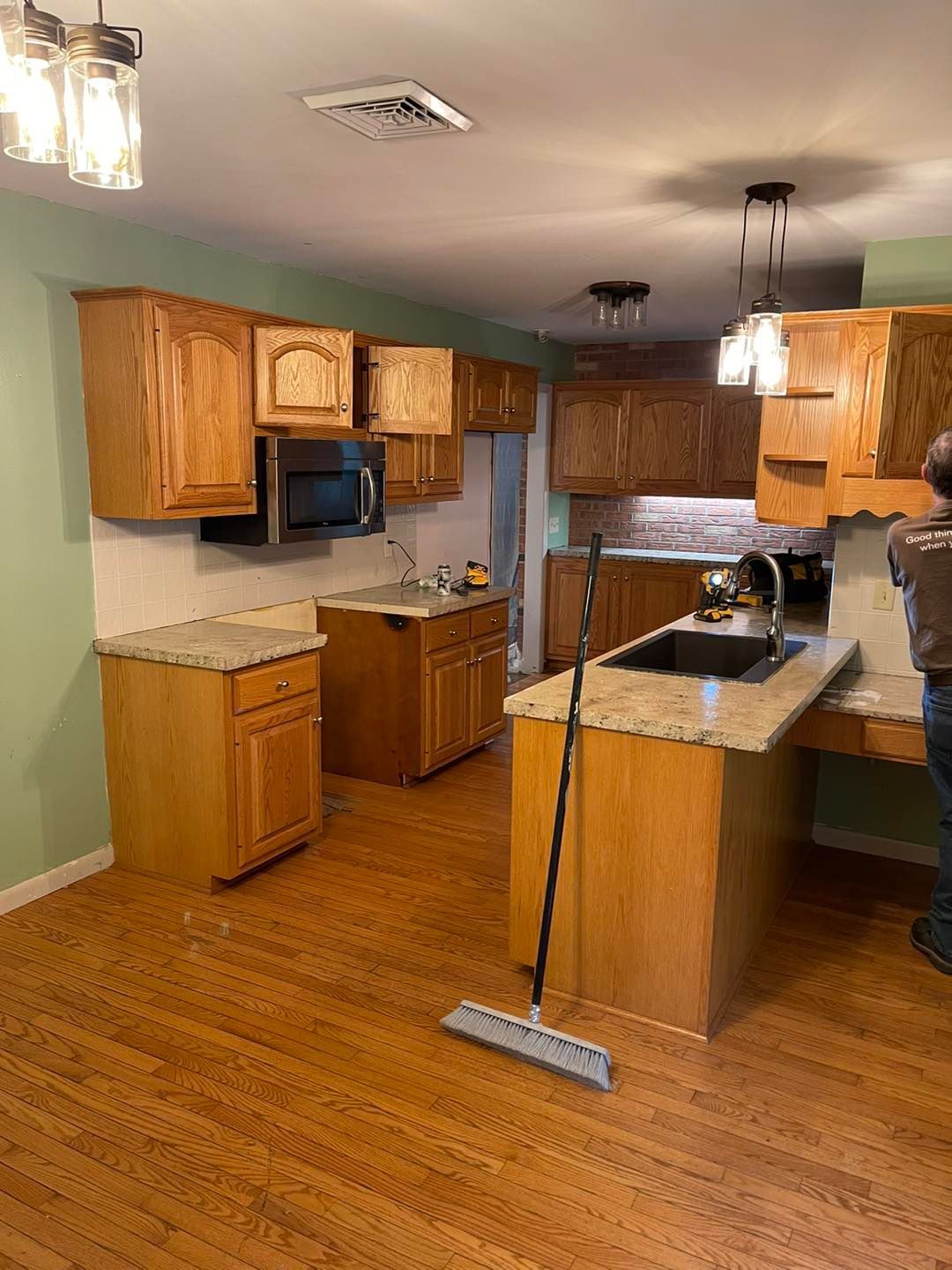 A kitchen with wood cabinets, tan countertops, and green walls. A person stands near the sink.