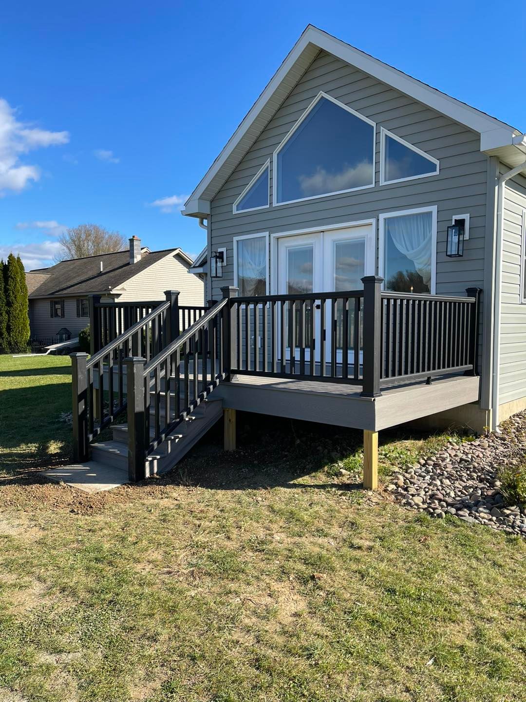 Gray deck with black railing leads to a gray house with large triangular windows.
