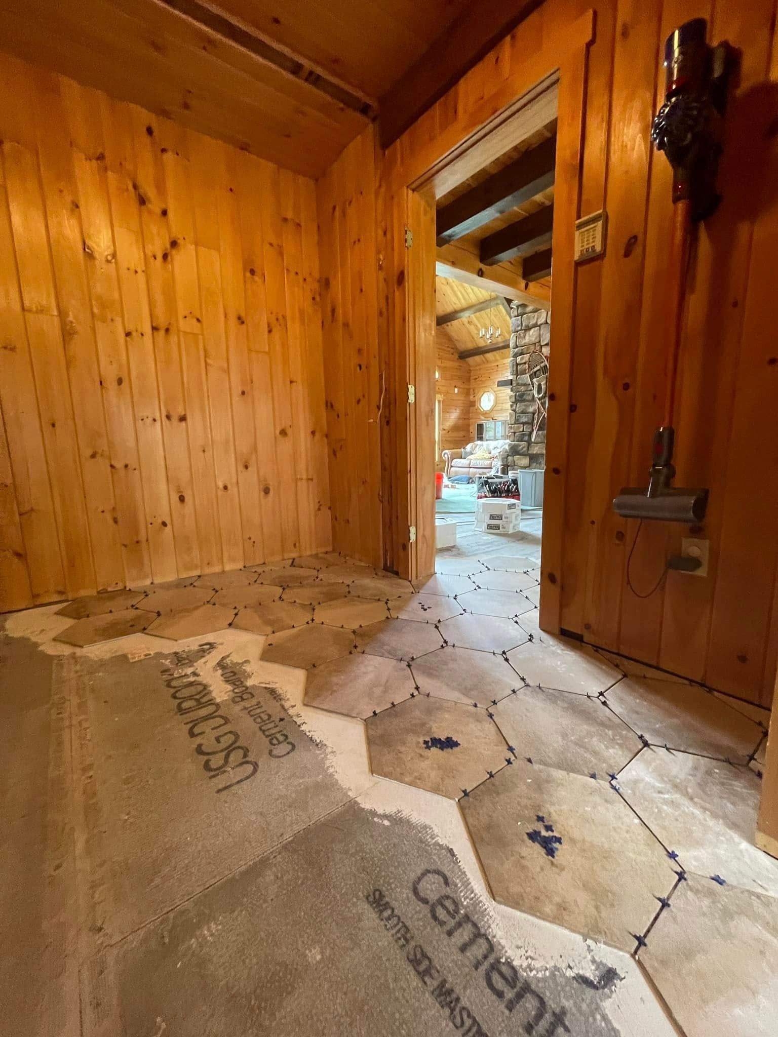 Entryway with wood paneling, doorway to another room, and unfinished floor with cement board.