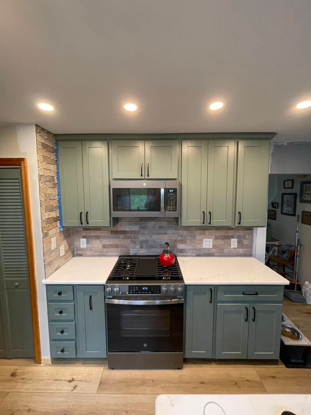 Green kitchen cabinets with a microwave, stove, and wood backsplash.