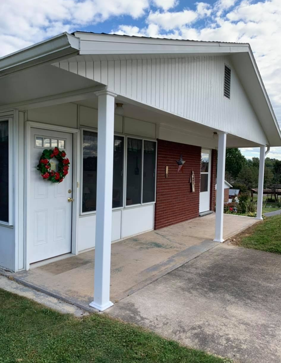 White house with porch, red brick wall, white pillars, and a wreath on the front door.