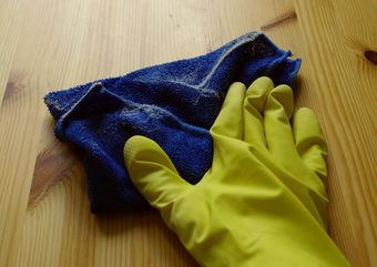 A person wearing yellow gloves is cleaning a wooden surface with a blue cloth