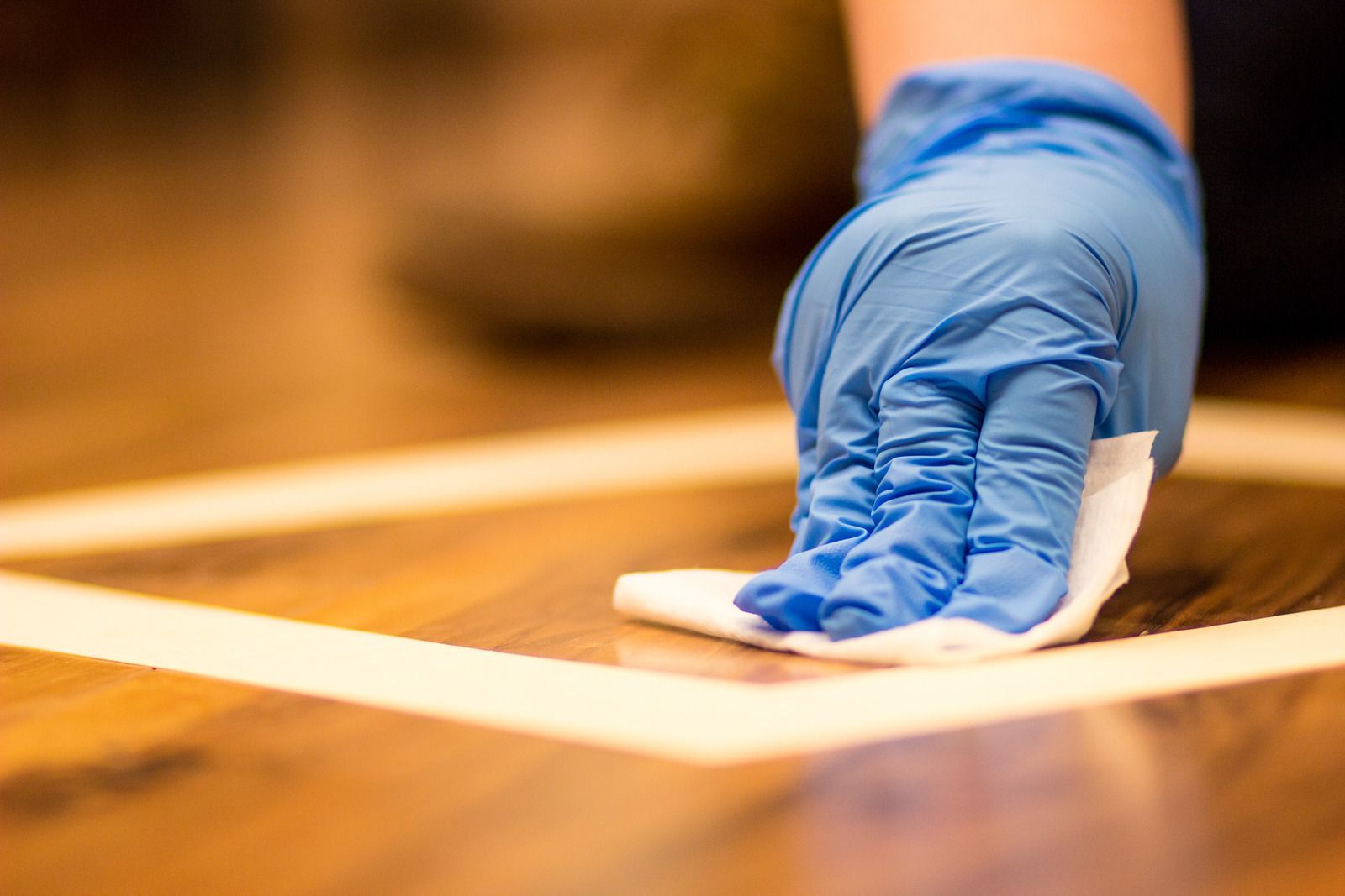 A person wearing blue gloves is cleaning a wooden floor with a cloth.
