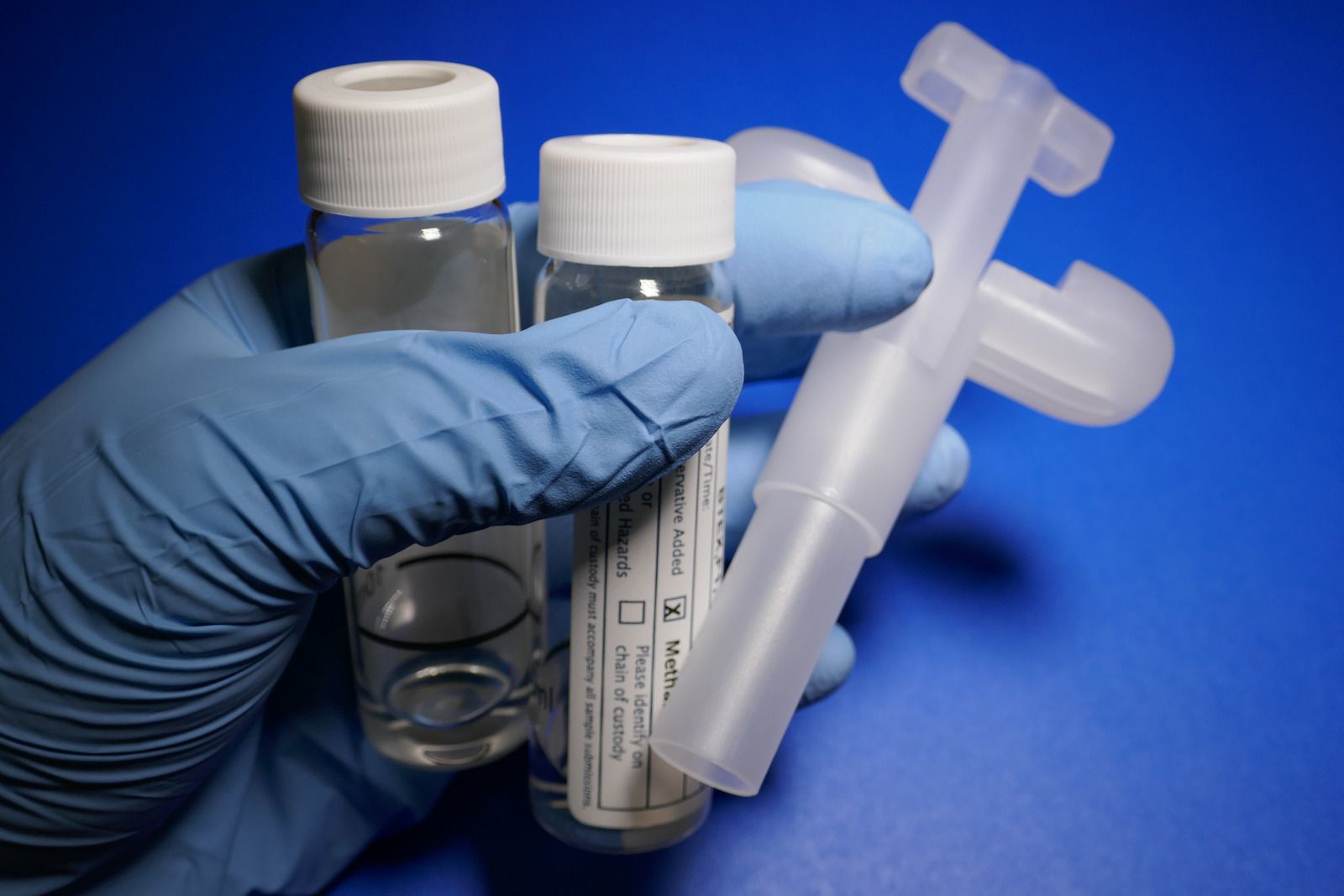 A person wearing blue gloves is holding two bottles and a syringe