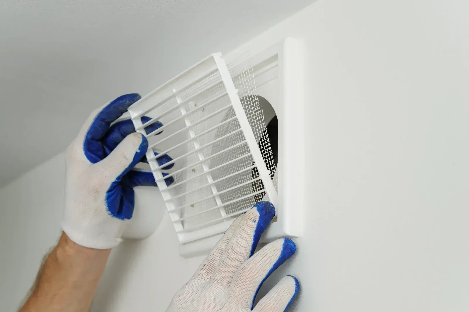 A person wearing blue gloves is installing a fan on a wall.
