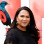 A woman is standing in front of a red sign with a bird in the background.