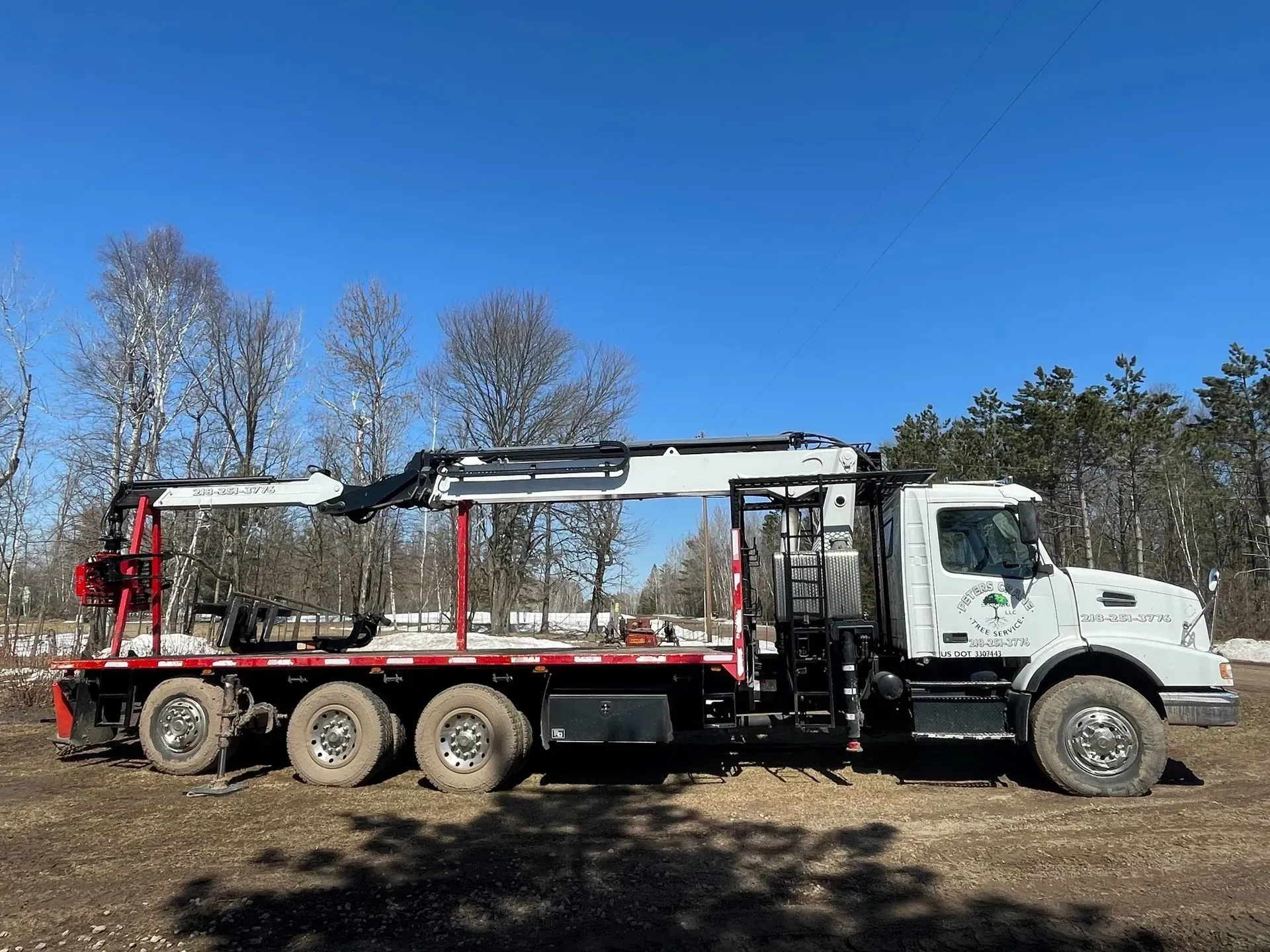 A truck with a crane on the back of it is parked in a dirt field.