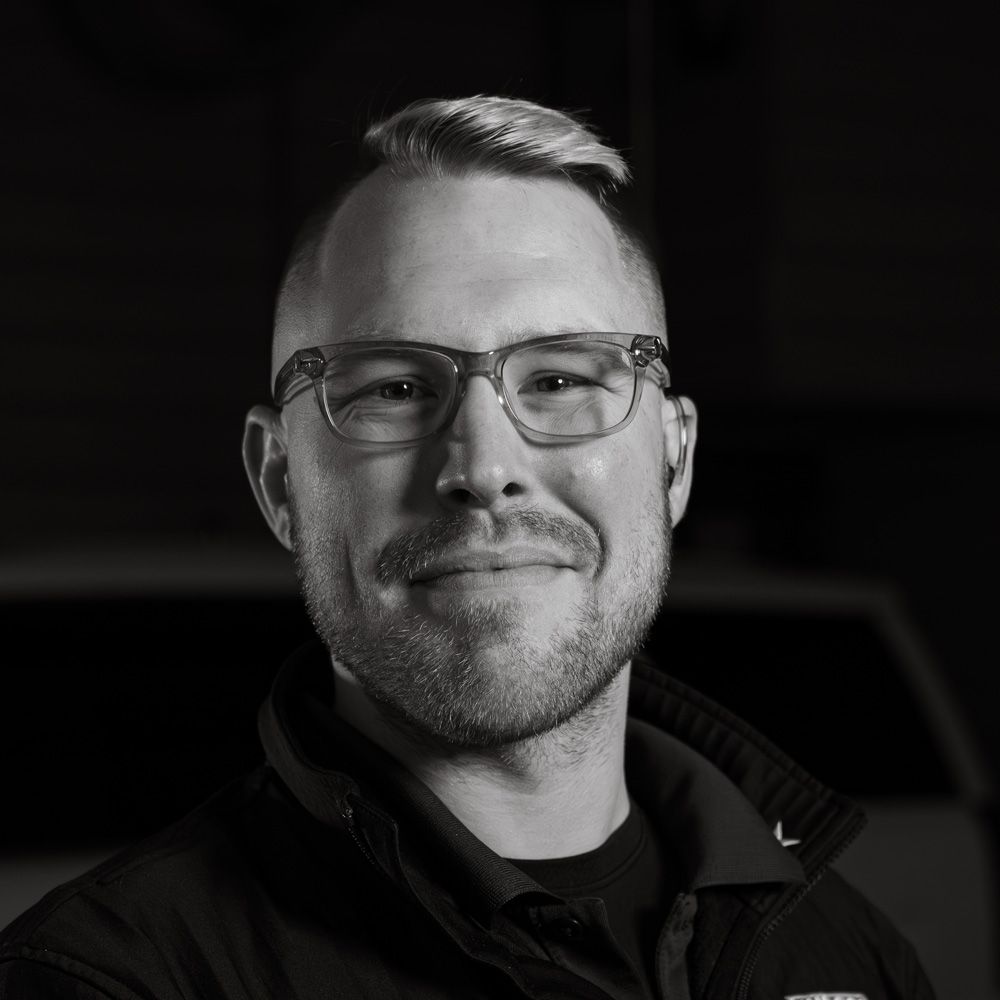 Black-and-white headshot of a smiling man wearing glasses and a dark jacket