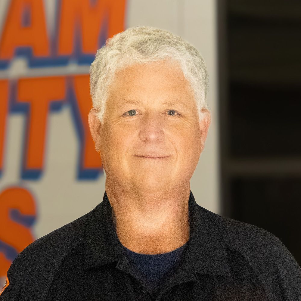 Portrait of a man with short white hair in a dark jacket, standing before a colorful studio backdrop