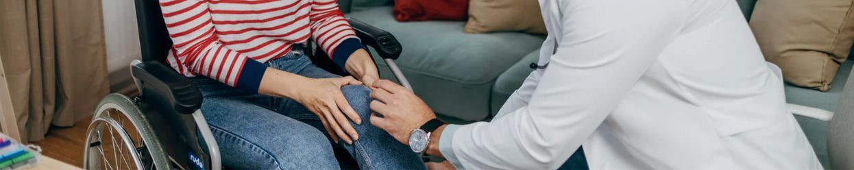Two people sitting closely on a couch, one in a red striped shirt, with a healthcare worker taking a pulse.