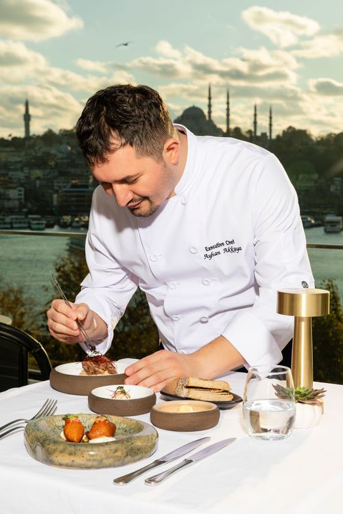 A man in a chef 's jacket is sitting at a table with plates of food, Ayhan Akkaya, Yuca restaurant