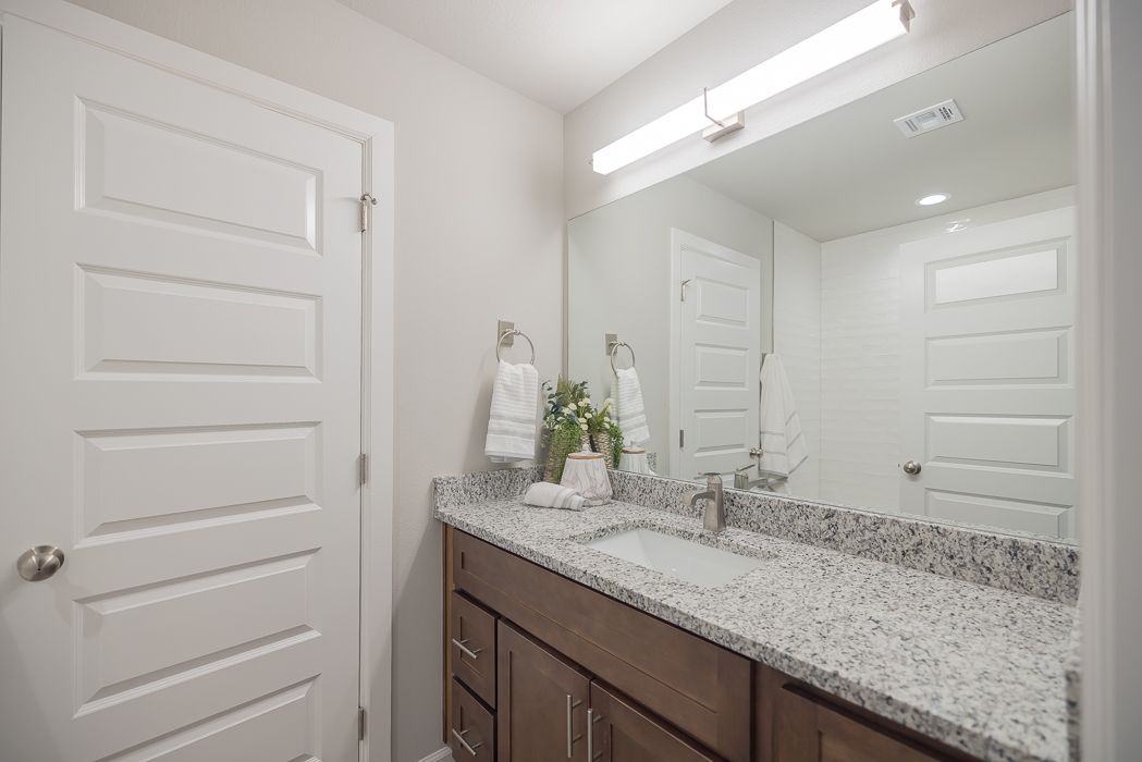 Bathroom with white door, grey granite countertop, mirror, and a brown vanity.