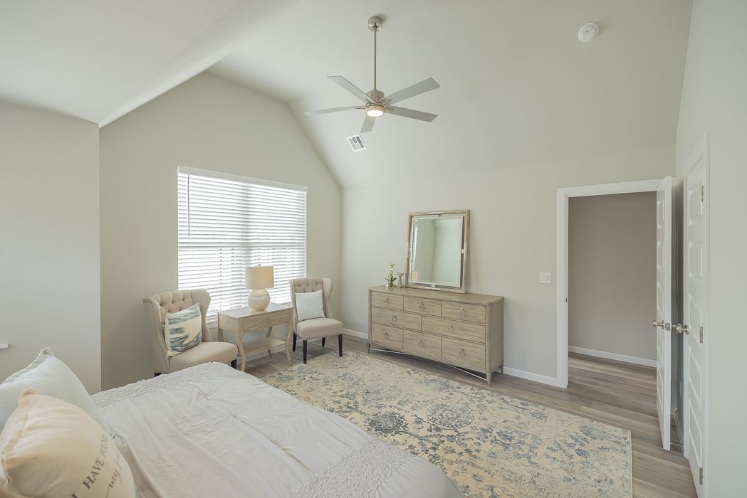 Bedroom with neutral tones; bed, dresser, chairs, rug, and a window with blinds.