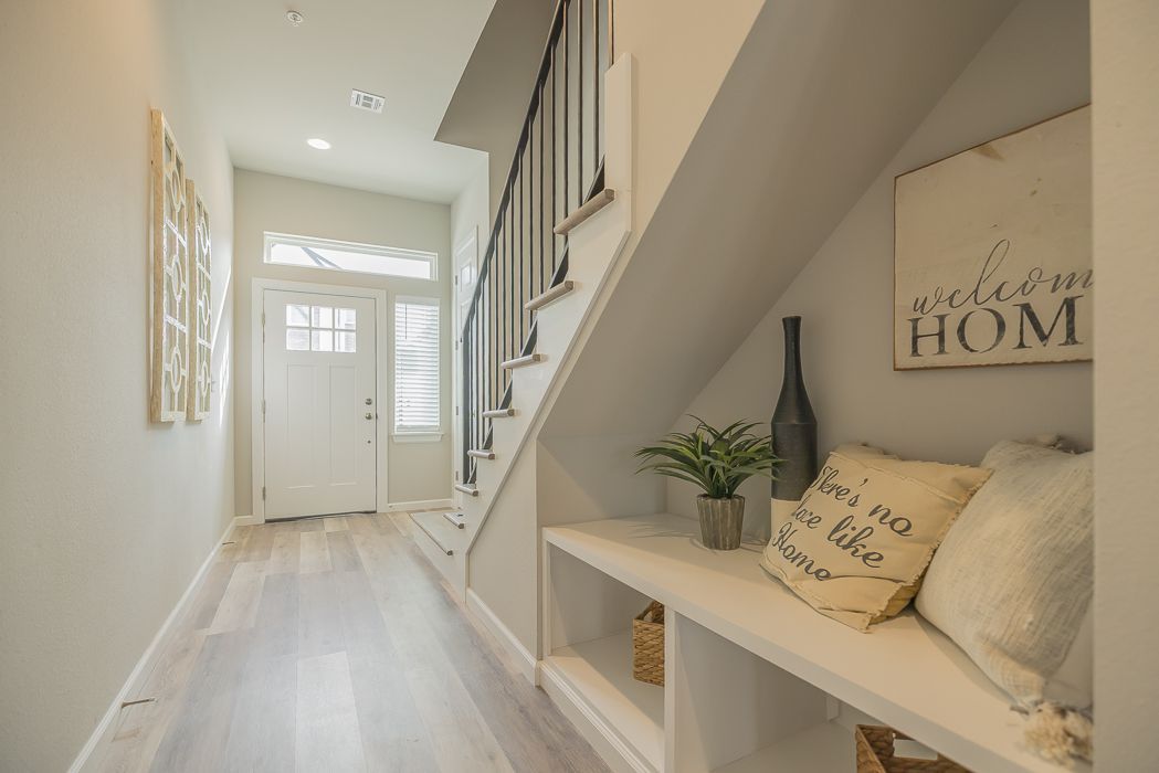 Narrow hallway with stairs, built-in storage, a door, and wooden floors. Light gray walls, a white door.