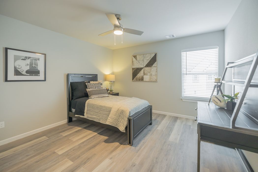 Bedroom with a twin bed, dresser, and light blue walls. Wood-look flooring, window with blinds, and artwork.