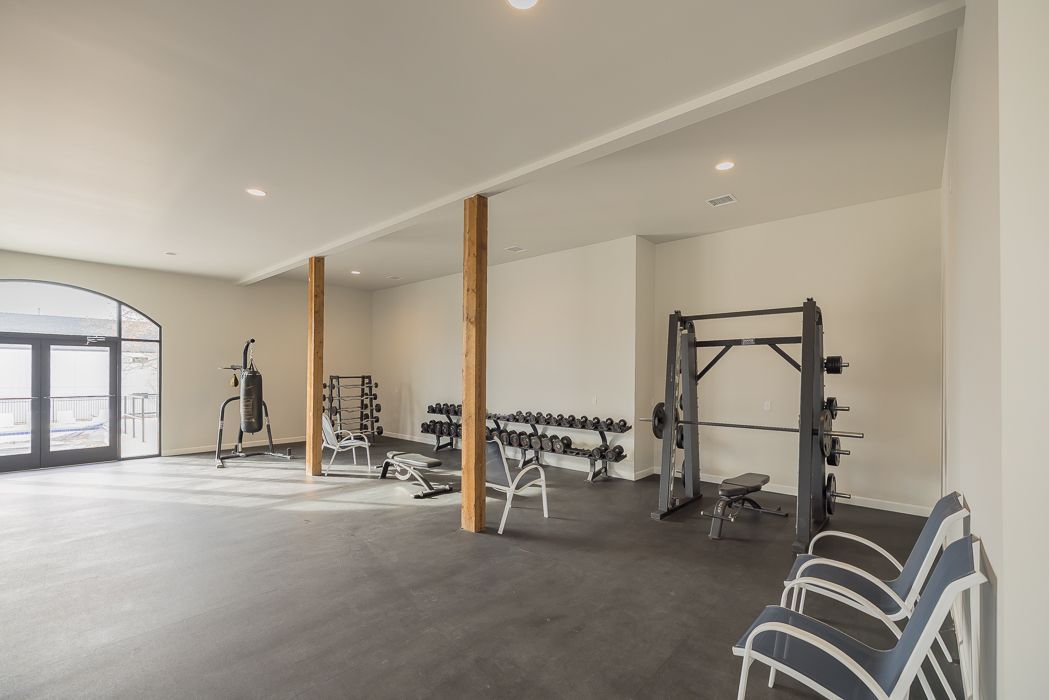 Gym with weights, exercise equipment, and chairs, featuring a dark floor and white walls.