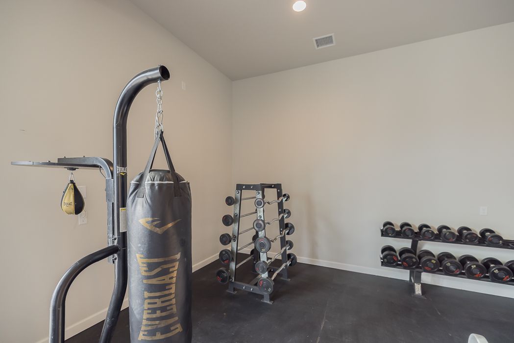 Home gym with punching bag, dumbbells, and weight rack on a black rubber floor.
