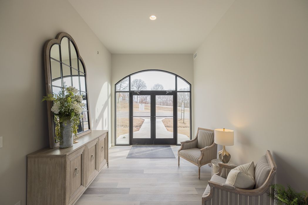 A bright entryway with a large mirror, console table, two chairs, and arched double doors leading outside.