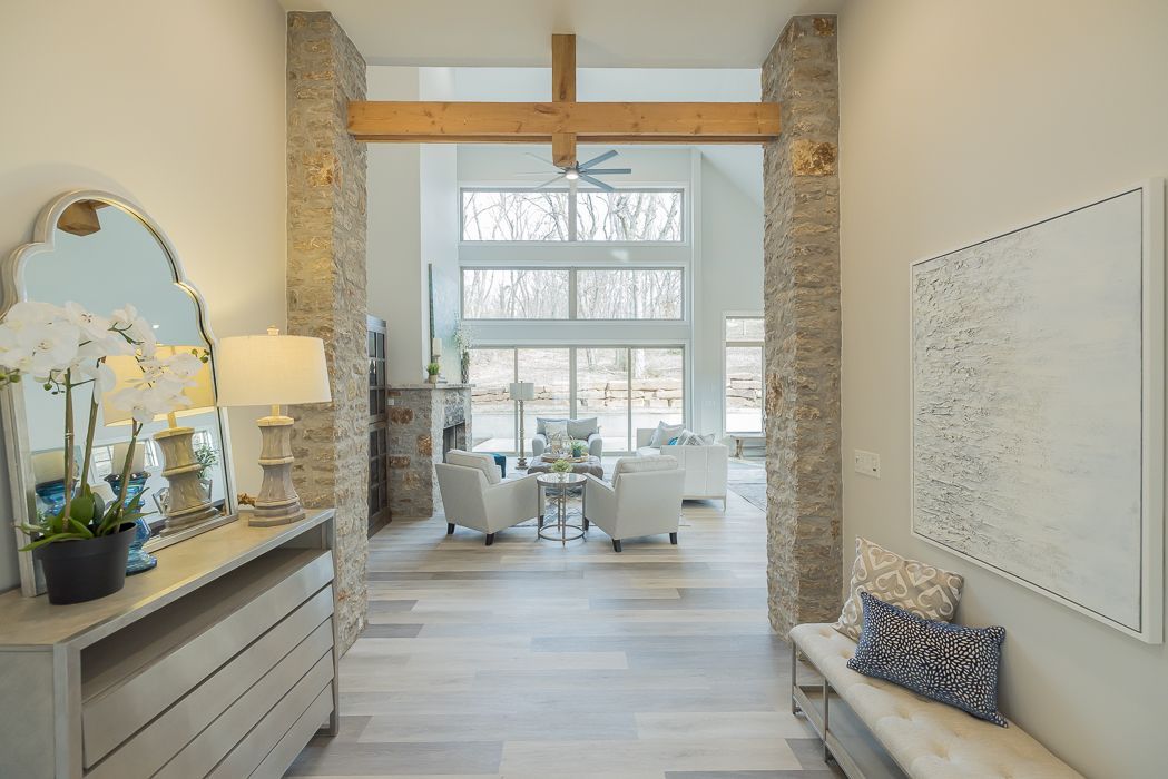 Entryway with stone columns, wooden beam, leading to a bright living room. Console with mirror, art on wall.