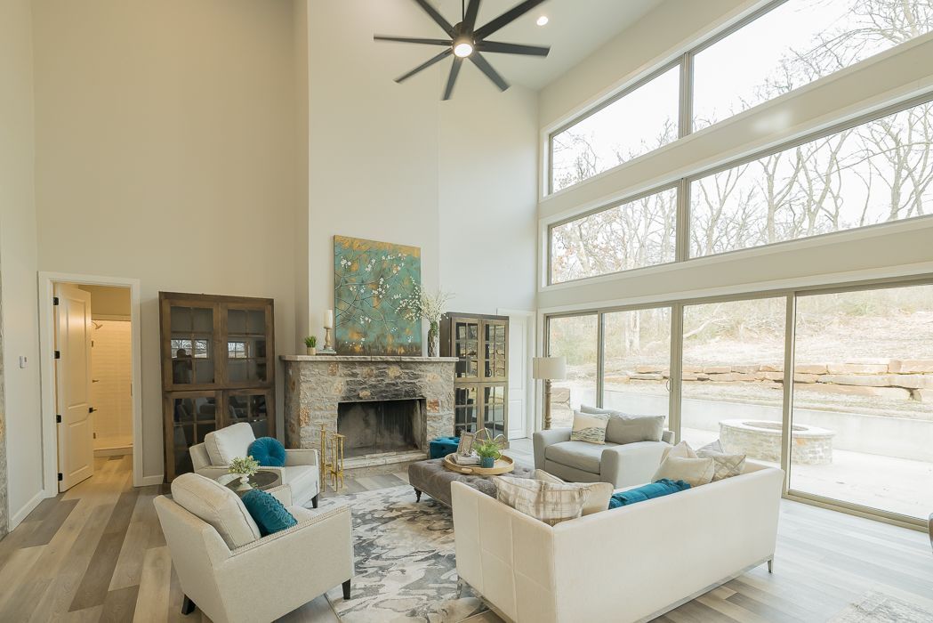 Spacious living room with high ceilings, fireplace, large windows, and light-colored furniture.
