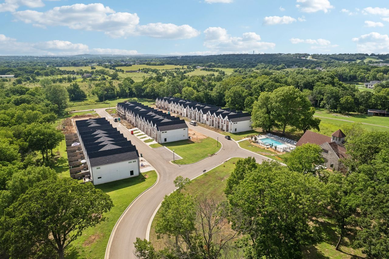 Aerial view of a housing development with white townhouses, black roofs, a pool, and green surroundings.