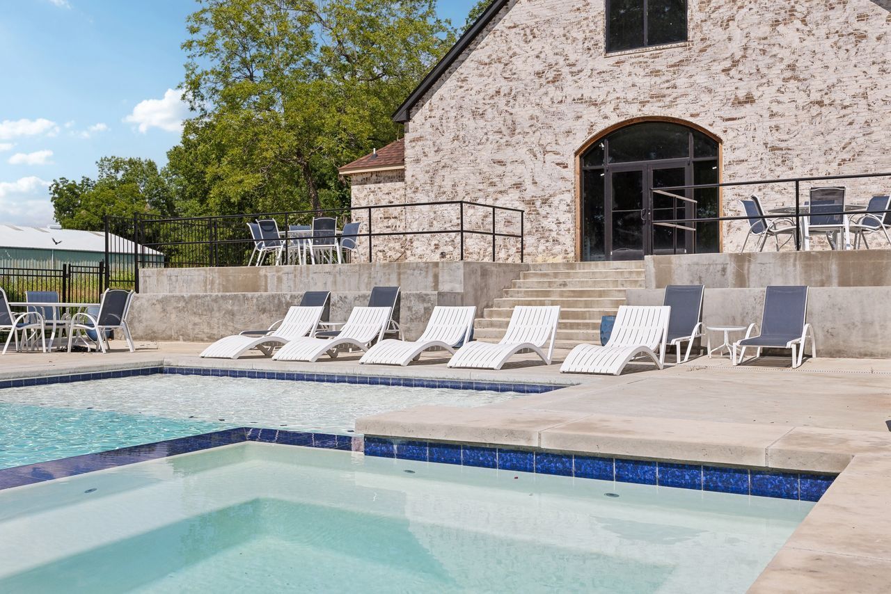 Poolside with lounge chairs in front of a stone building and blue sky.