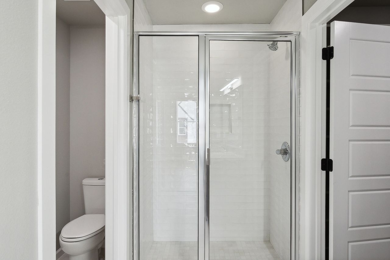 Bathroom with a shower, toilet, and white door. The shower has a glass door.