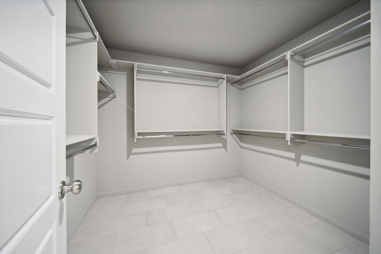 Empty white walk-in closet with shelves and hanging rods; a door on the left.